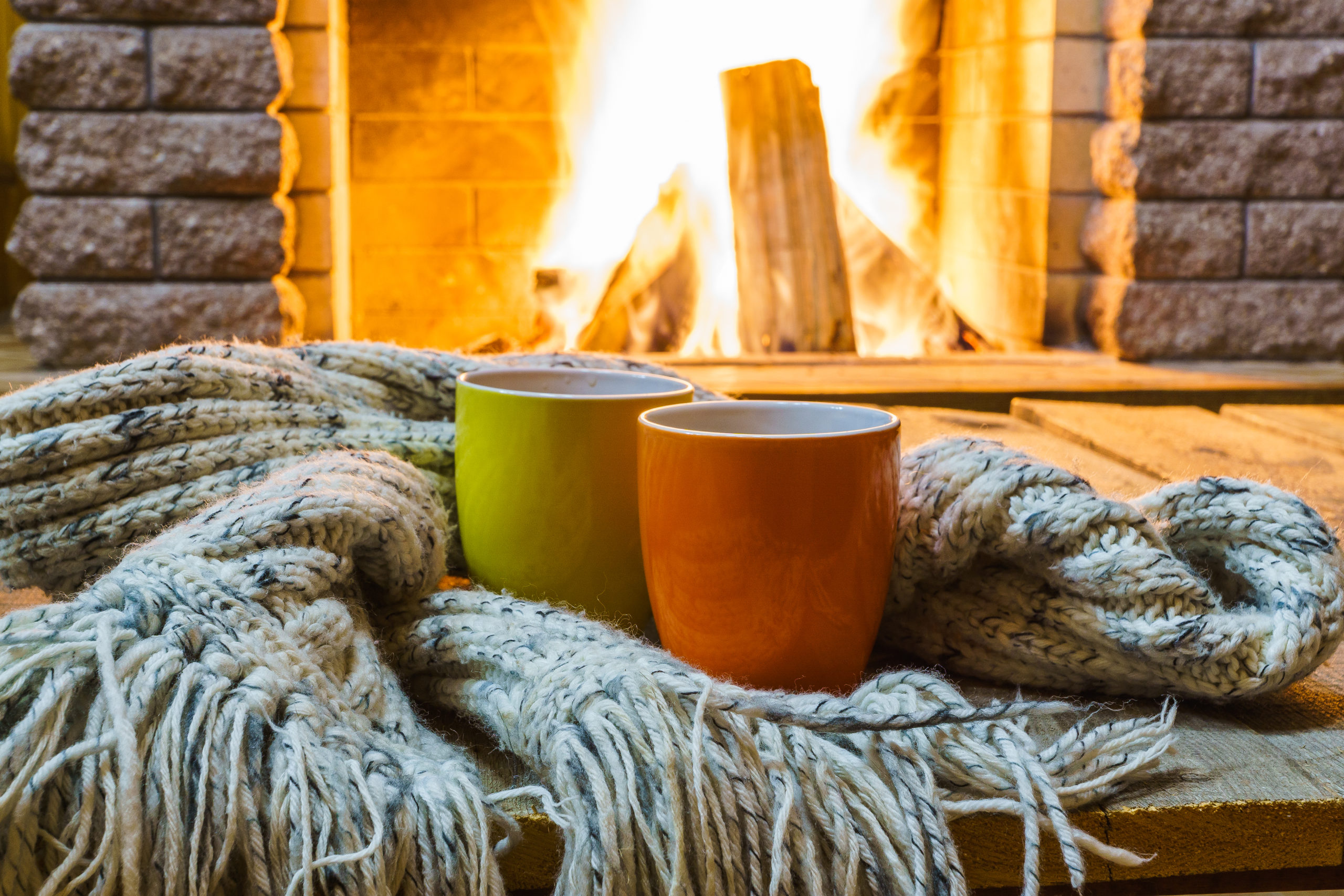 Mugs  for tea or coffee,  wool things near cozy fireplace, in country house, winter vacation, horizontal.
